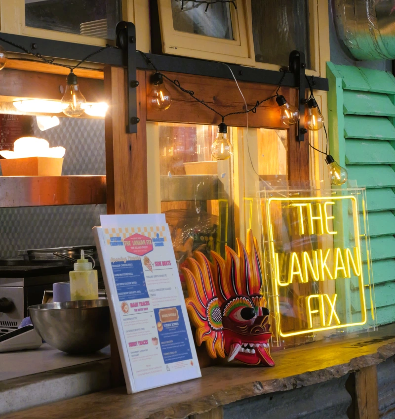 The Lankan Fix kitchen takeover setup with neon sign, menu and Sri Lankan mask.
